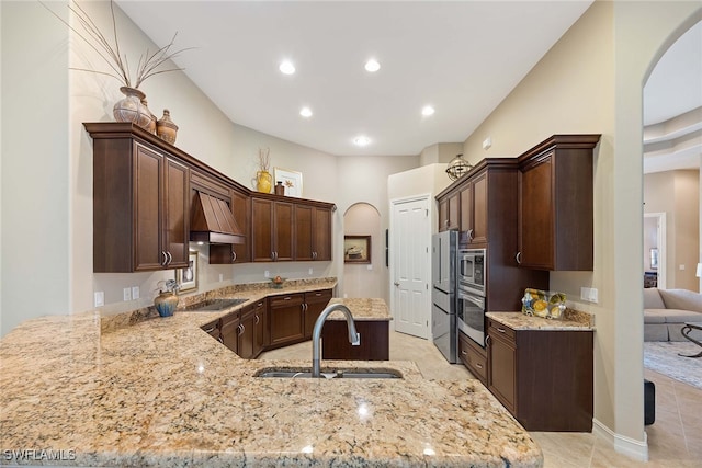 kitchen with light stone countertops, custom range hood, kitchen peninsula, and stainless steel appliances