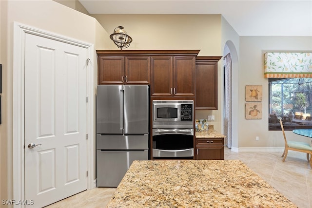 kitchen with appliances with stainless steel finishes, dark brown cabinetry, light tile patterned flooring, and light stone countertops