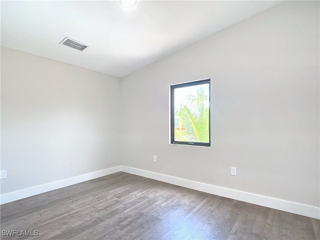 empty room with visible vents, baseboards, dark wood-style floors, and vaulted ceiling