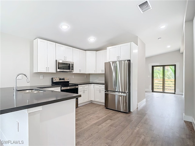 kitchen with light wood-type flooring, appliances with stainless steel finishes, sink, lofted ceiling, and kitchen peninsula