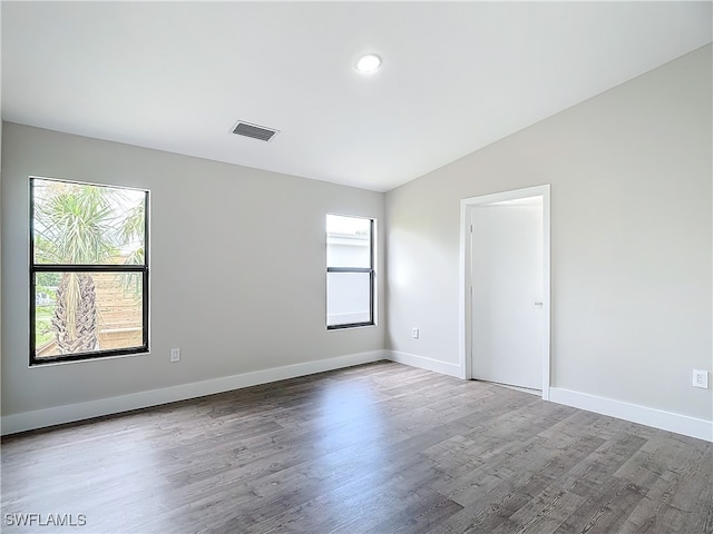 empty room featuring lofted ceiling, wood finished floors, a healthy amount of sunlight, and visible vents