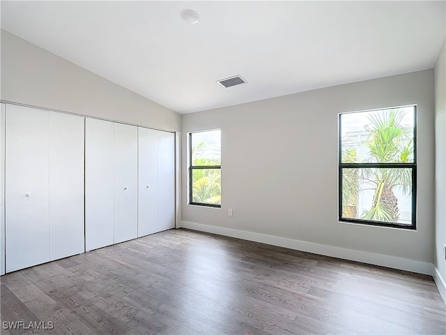 unfurnished bedroom with wood finished floors, visible vents, baseboards, vaulted ceiling, and a closet