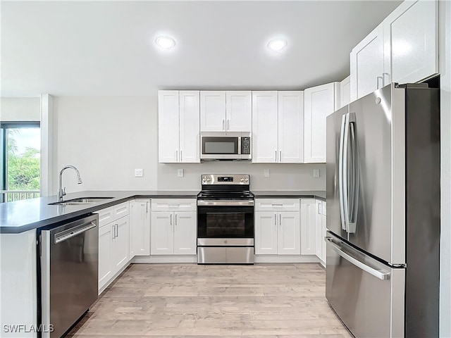 kitchen with stainless steel appliances, sink, kitchen peninsula, light wood-type flooring, and white cabinets