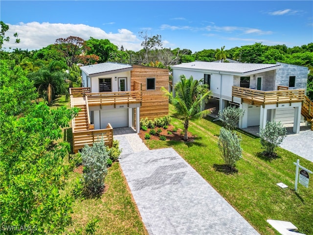 modern home featuring stairs, a front yard, an attached garage, and decorative driveway