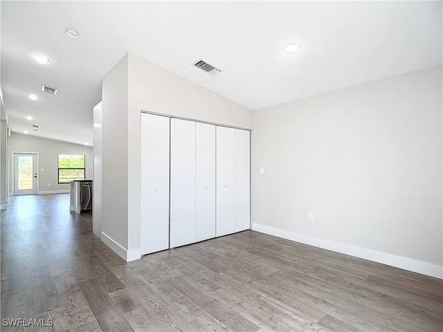 unfurnished bedroom featuring visible vents, lofted ceiling, baseboards, and wood finished floors