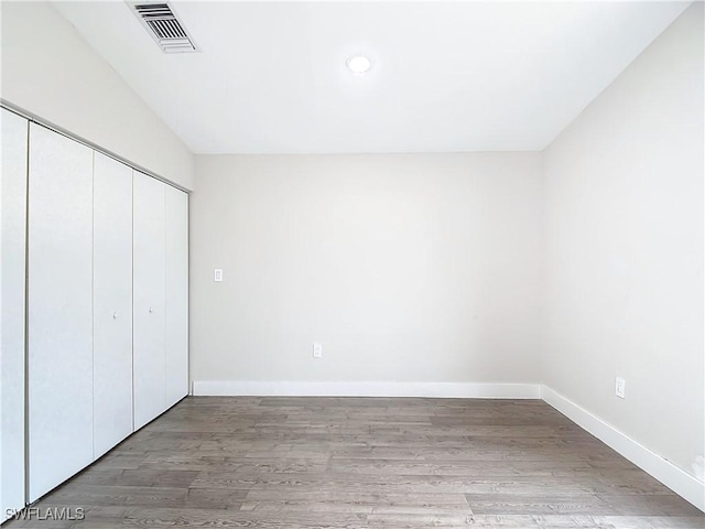 unfurnished bedroom featuring a closet, visible vents, baseboards, and wood finished floors