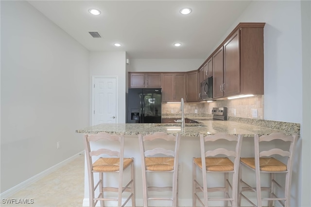 kitchen featuring a kitchen bar, black appliances, light stone countertops, and decorative backsplash