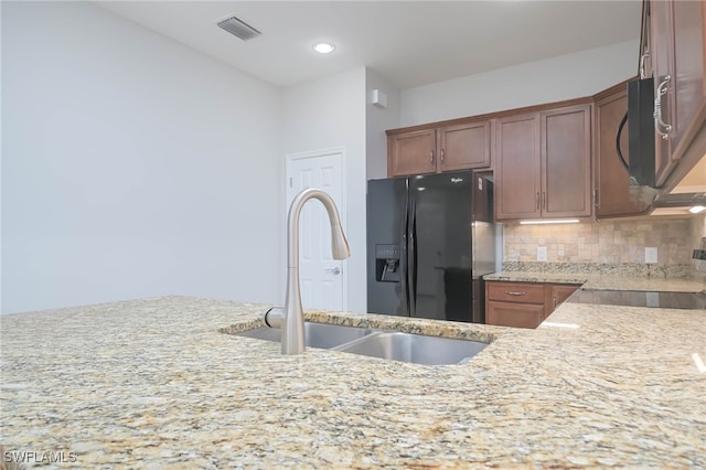 kitchen with black appliances, backsplash, light stone countertops, and sink