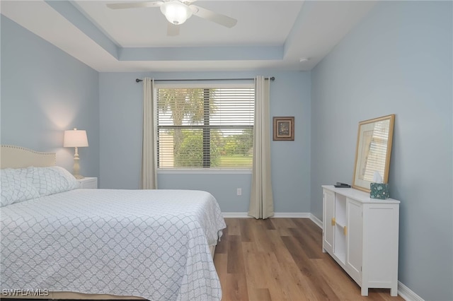 bedroom with ceiling fan, light wood-type flooring, and a tray ceiling