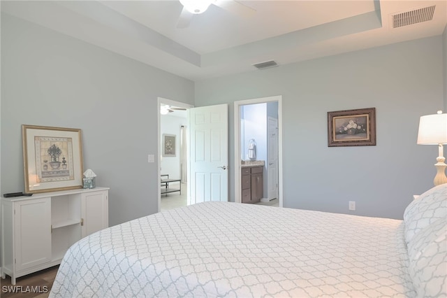 bedroom with a tray ceiling, ceiling fan, and ensuite bath