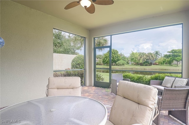 sunroom / solarium with a healthy amount of sunlight, ceiling fan, and a water view