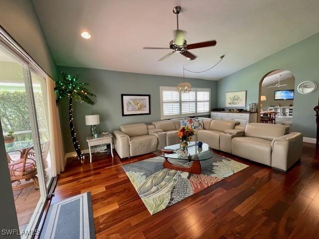 living room with ceiling fan with notable chandelier, vaulted ceiling, and dark hardwood / wood-style flooring