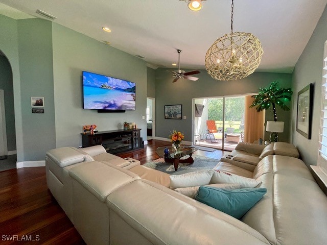 living room featuring ceiling fan with notable chandelier, dark wood-type flooring, and vaulted ceiling