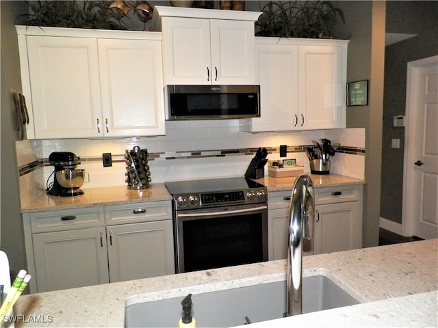 kitchen featuring white cabinets, appliances with stainless steel finishes, light stone countertops, and tasteful backsplash