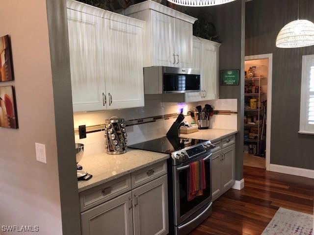 kitchen featuring dark hardwood / wood-style floors, white cabinetry, backsplash, stainless steel appliances, and light stone countertops