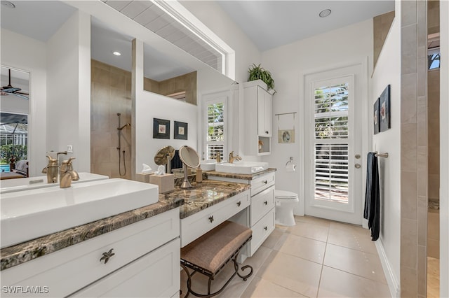 bathroom featuring toilet, tile patterned flooring, vanity, tiled shower, and ceiling fan