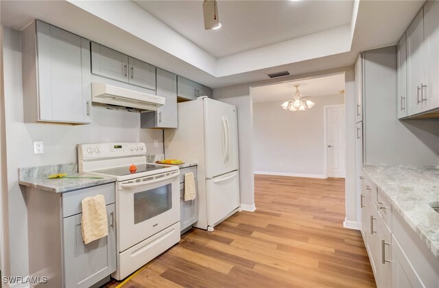 kitchen featuring light stone counters, white appliances, decorative light fixtures, a notable chandelier, and light hardwood / wood-style floors