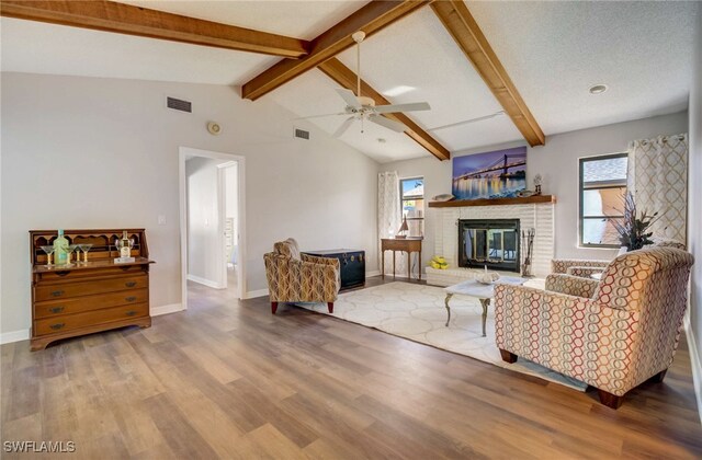 living room featuring a fireplace, a textured ceiling, ceiling fan, hardwood / wood-style flooring, and vaulted ceiling with beams