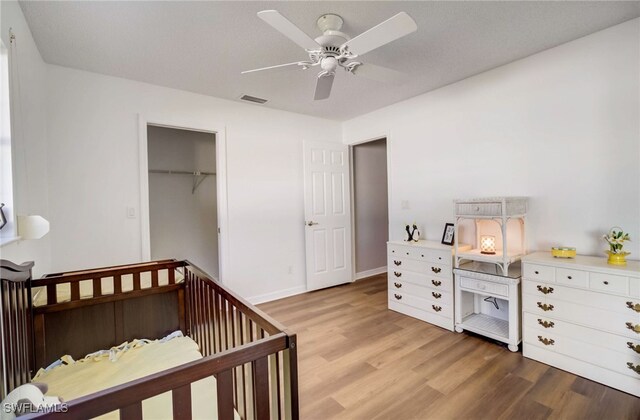 bedroom with a closet, light hardwood / wood-style floors, a crib, and ceiling fan