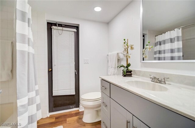 bathroom with hardwood / wood-style floors, walk in shower, vanity, and toilet