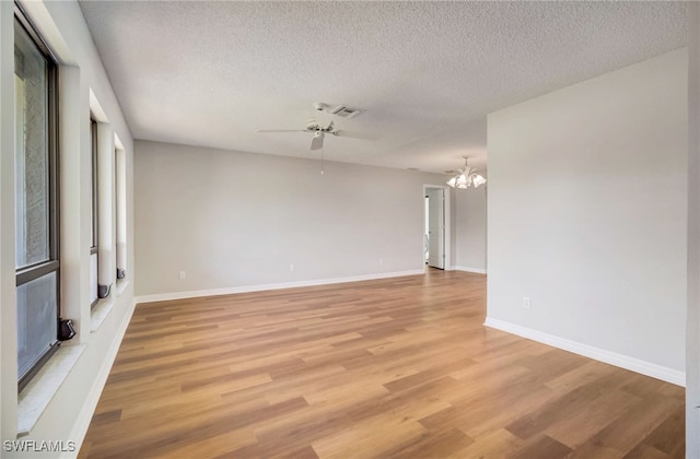 empty room with ceiling fan with notable chandelier, a textured ceiling, and light wood-type flooring