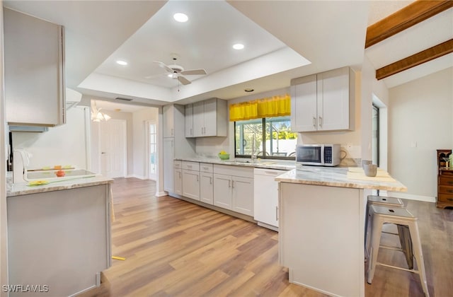 kitchen featuring light wood-type flooring, kitchen peninsula, a kitchen breakfast bar, white appliances, and ceiling fan