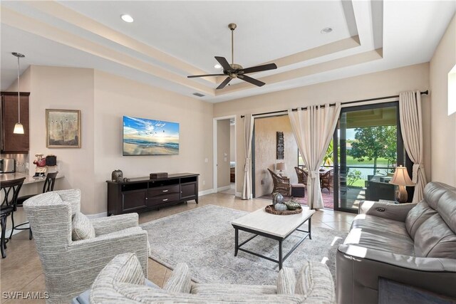 tiled living room featuring ceiling fan and a tray ceiling