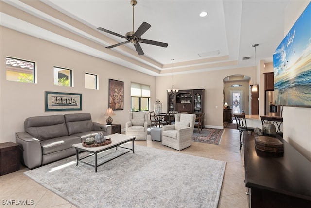 living room featuring a raised ceiling, light tile patterned floors, and ceiling fan with notable chandelier