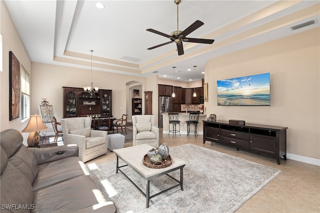 tiled living room featuring a raised ceiling and ceiling fan with notable chandelier