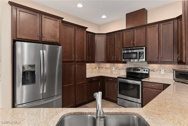 kitchen with tasteful backsplash, light stone countertops, stainless steel appliances, and dark brown cabinetry