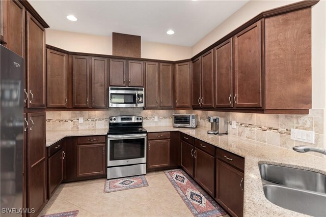 kitchen with light stone countertops, appliances with stainless steel finishes, sink, and dark brown cabinets