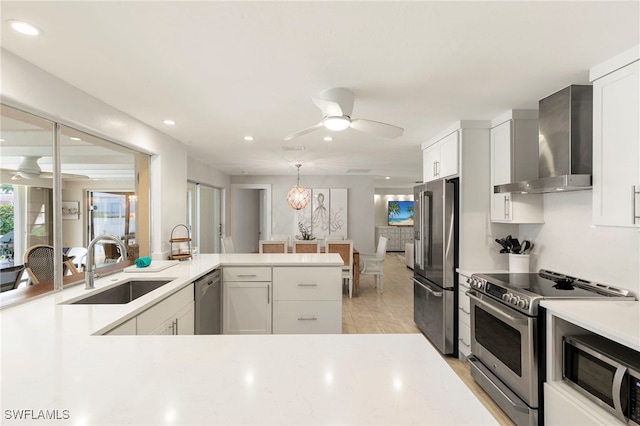 kitchen featuring ceiling fan, wall chimney exhaust hood, stainless steel appliances, light countertops, and a sink