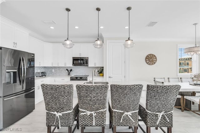 kitchen with pendant lighting, tasteful backsplash, light countertops, appliances with stainless steel finishes, and white cabinets