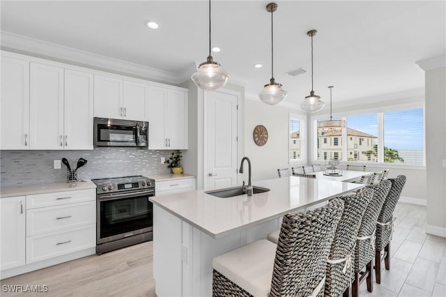 kitchen featuring stainless steel appliances, a sink, white cabinetry, light countertops, and an island with sink