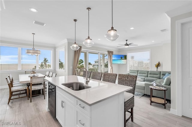 kitchen with a sink, white cabinets, open floor plan, light countertops, and a center island with sink