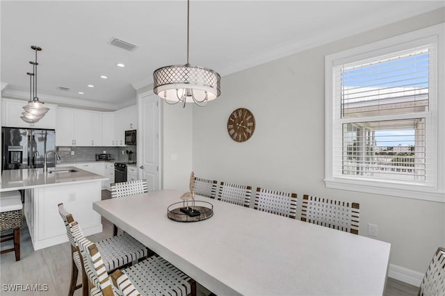 dining room with light wood finished floors, baseboards, visible vents, and crown molding