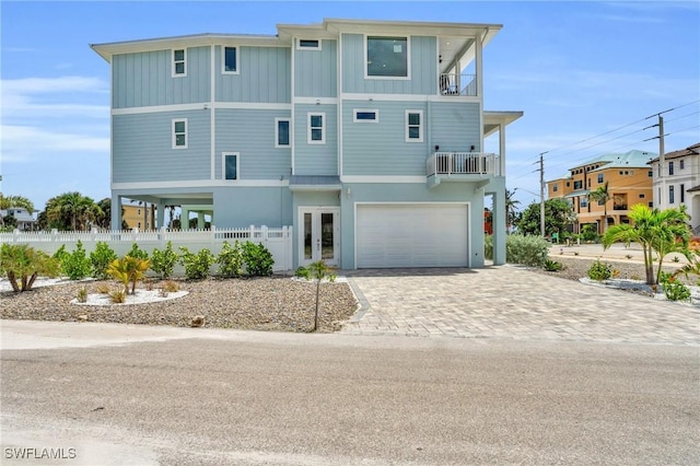 coastal home with an attached garage, a balcony, fence, decorative driveway, and board and batten siding