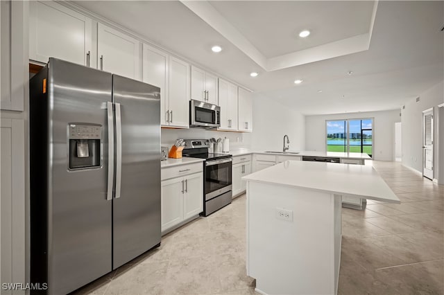 kitchen featuring white cabinetry, stainless steel appliances, kitchen peninsula, sink, and a tray ceiling