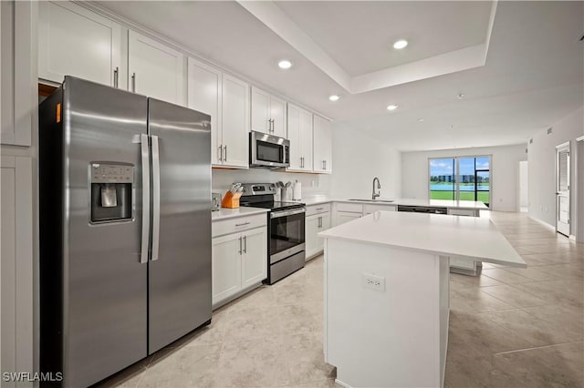 kitchen with stainless steel appliances, a peninsula, a sink, light countertops, and a center island