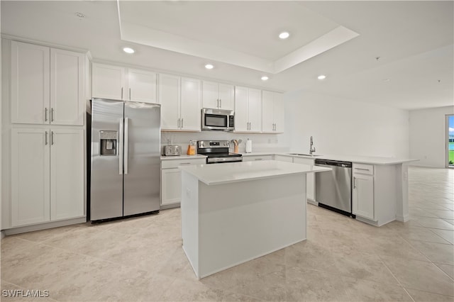 kitchen with appliances with stainless steel finishes, white cabinetry, sink, a tray ceiling, and a kitchen island