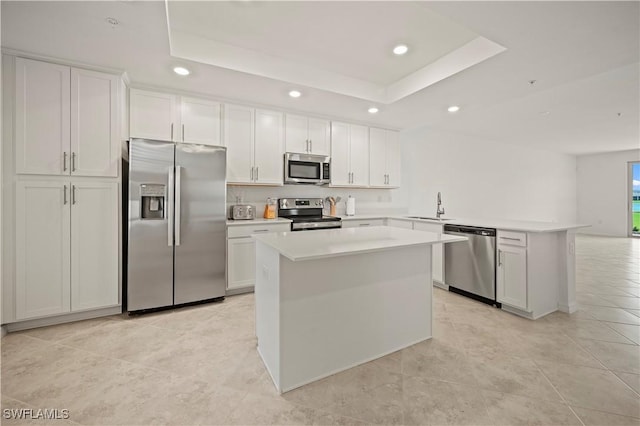 kitchen featuring a tray ceiling, recessed lighting, appliances with stainless steel finishes, a sink, and a peninsula