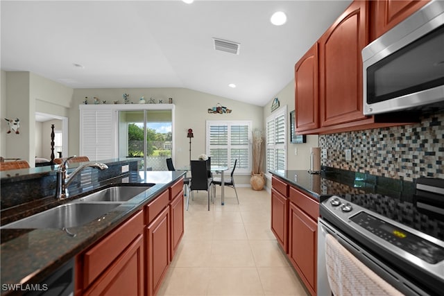 kitchen with lofted ceiling, sink, dark stone countertops, stainless steel appliances, and tasteful backsplash