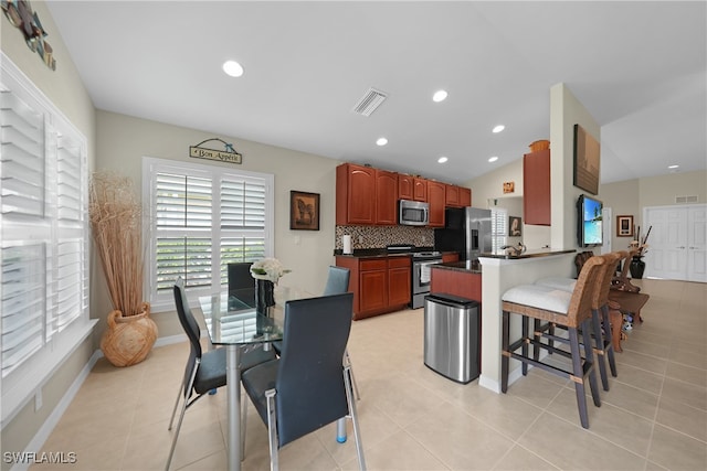 kitchen with light tile patterned flooring, tasteful backsplash, a kitchen bar, kitchen peninsula, and stainless steel appliances