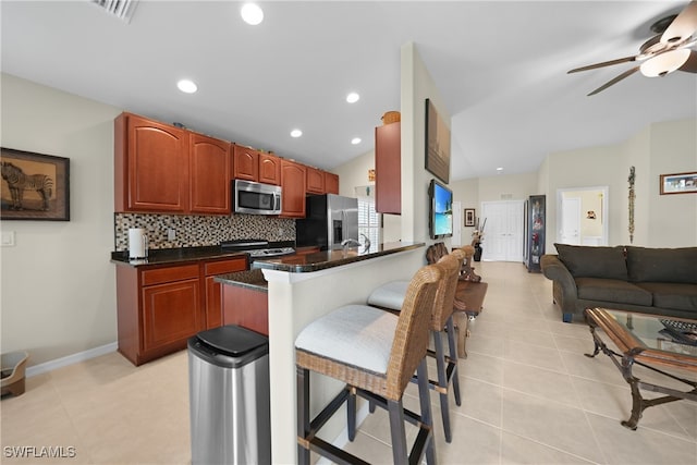 kitchen featuring vaulted ceiling, appliances with stainless steel finishes, a breakfast bar, backsplash, and kitchen peninsula