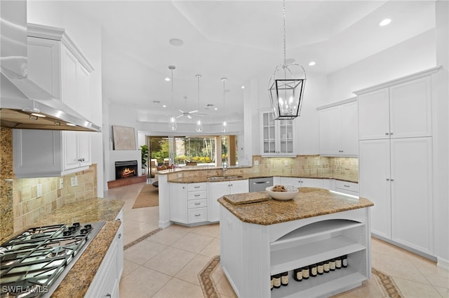 kitchen with kitchen peninsula, appliances with stainless steel finishes, backsplash, wall chimney range hood, and a kitchen island