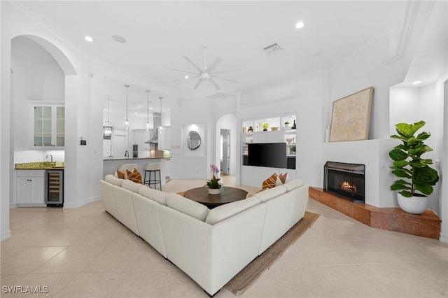 living room featuring ceiling fan, sink, beverage cooler, crown molding, and light tile patterned floors