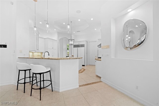 kitchen featuring kitchen peninsula, light stone counters, pendant lighting, white cabinetry, and light tile patterned flooring