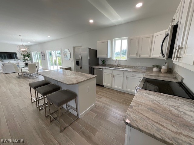 kitchen featuring sink, stainless steel appliances, light stone countertops, white cabinets, and a kitchen island