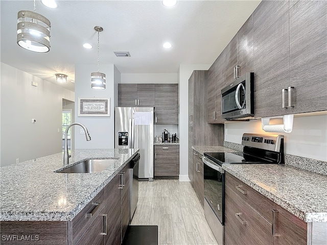 kitchen with a center island with sink, pendant lighting, appliances with stainless steel finishes, sink, and light wood-type flooring