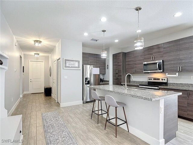 kitchen featuring hanging light fixtures, appliances with stainless steel finishes, light hardwood / wood-style floors, a center island with sink, and a breakfast bar